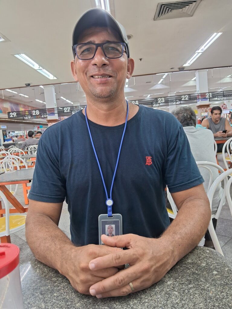 Bruno Teixeira sorrindo, de boné, óculos e crachá de identificação da Segel