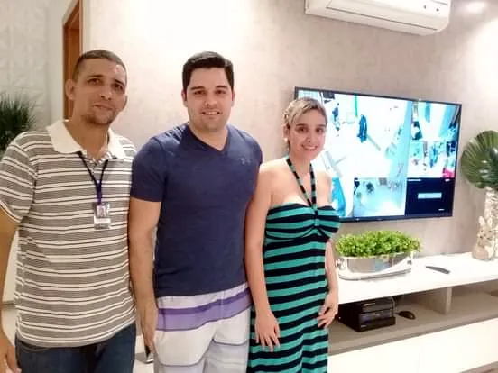 Bruno com casal de clientes ao lado da TV com as 4 câmeras do apartamento