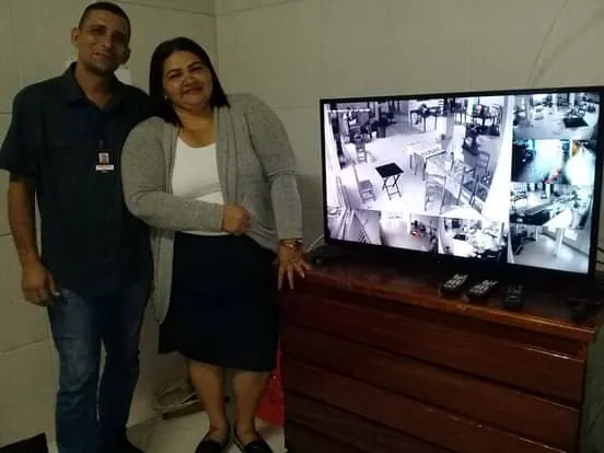 Bruno com a proprietária de empresa de alimentos ao lado do monitor com 16 câmeras